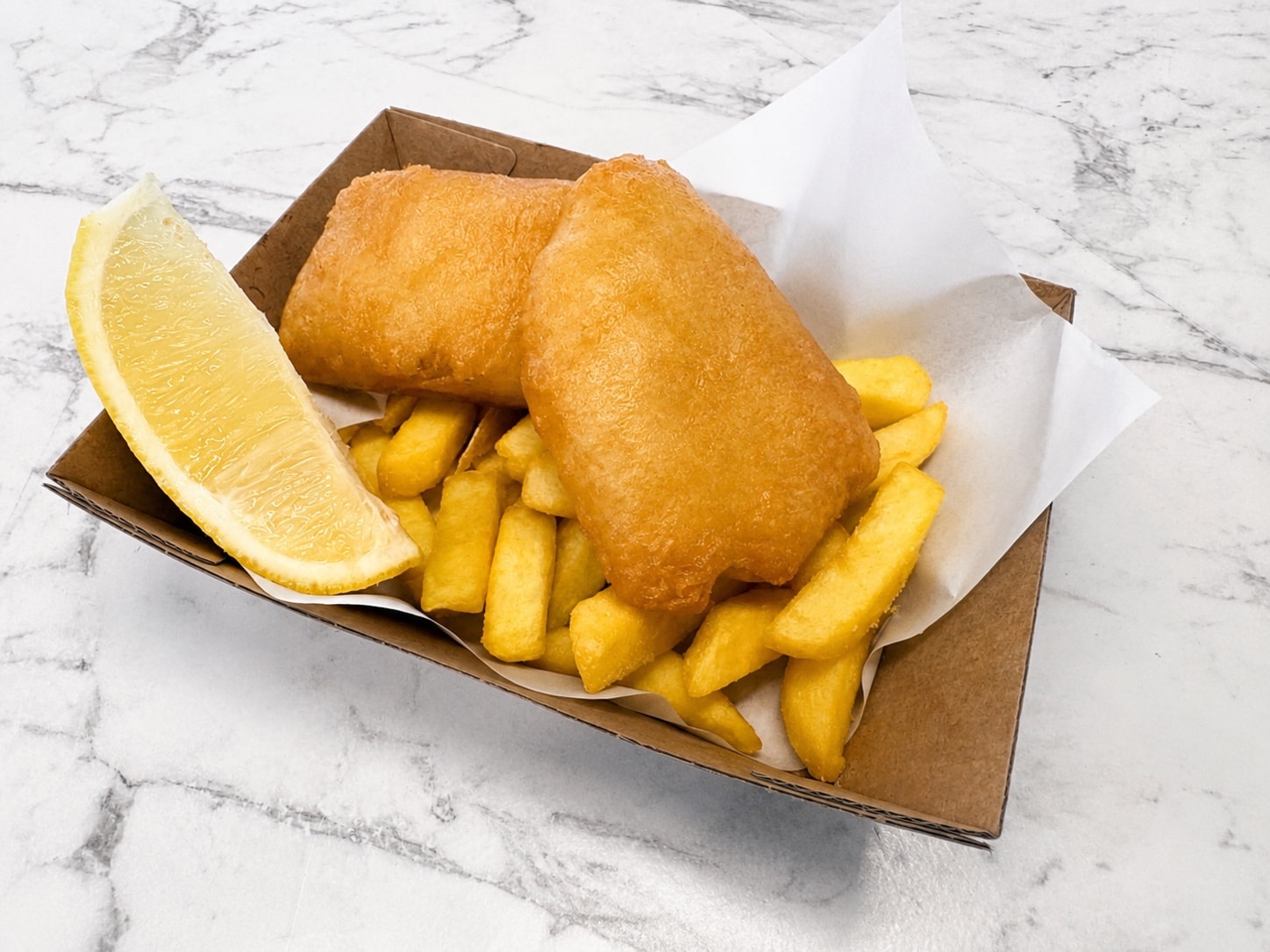 Kids' light and crispy battered fish and chips with a lemon wedge